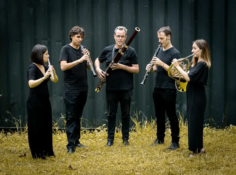 El quinteto tocando junto a una pared oscura, entre la hierba